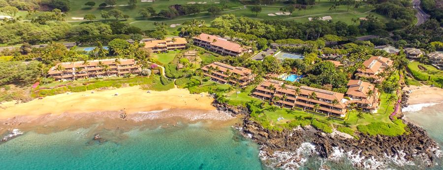 Aerial view of Makena Surf's buildings along the lava-rock shoreline, with beaches on either side